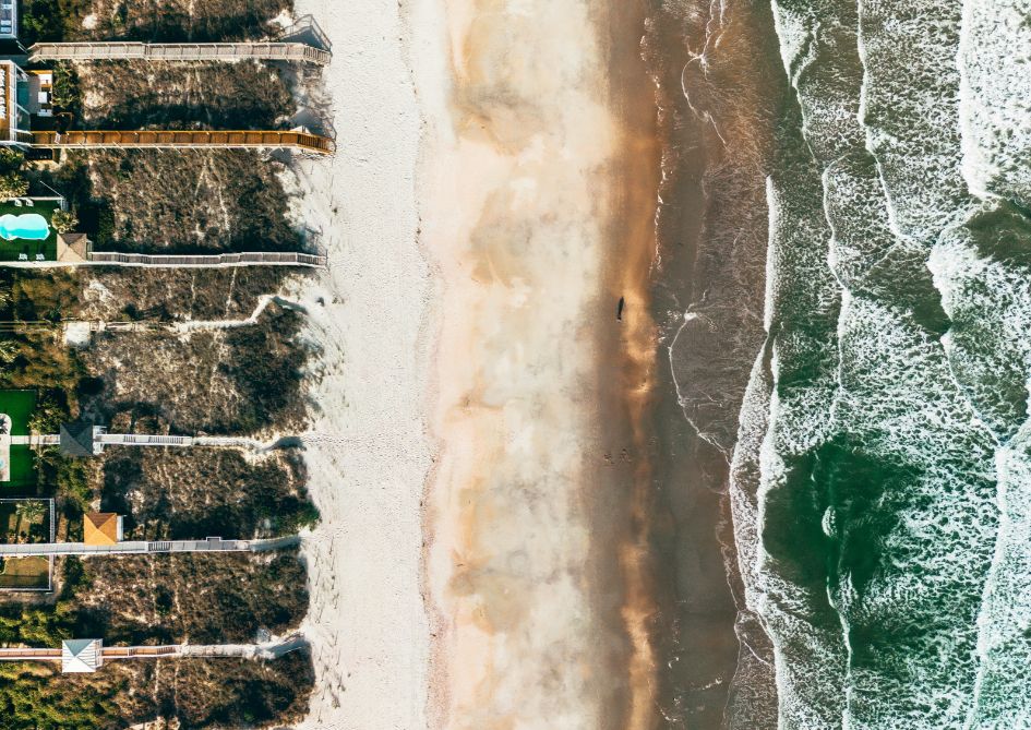 Aerial view of a beach with waves lapping at the shore and colorful houses lining the coastline.
